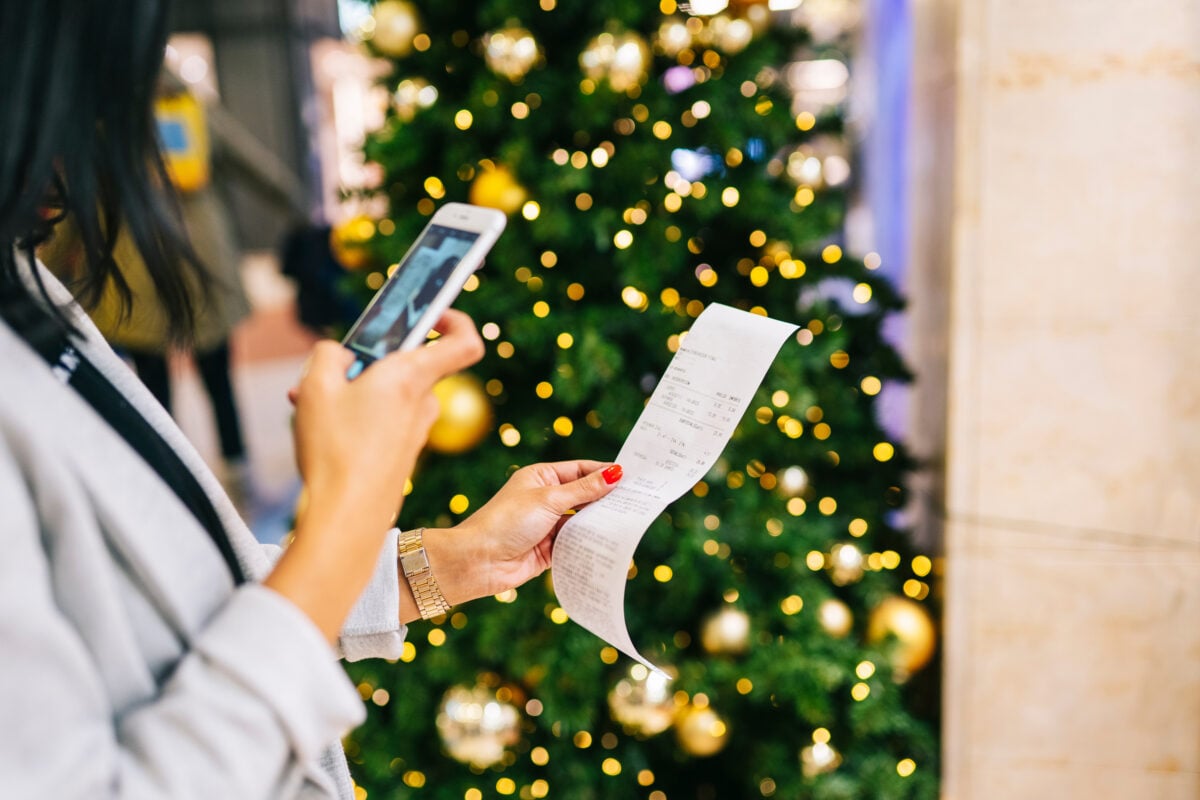 A woman taking a photo of a supermarket receipt next to a brightly lit Christmas tree