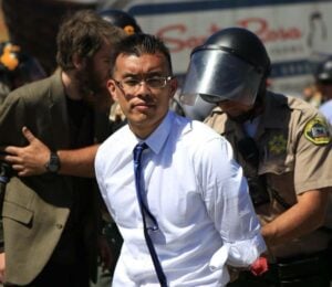 Direct Action Everywhere animal activist Wayne Hsiung being held in handcuffs by police