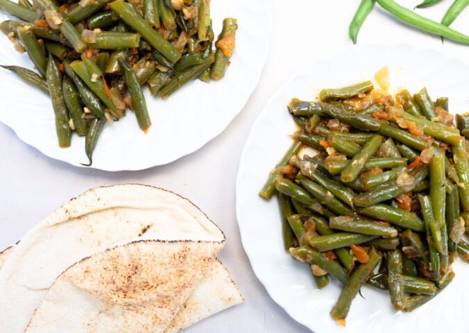 Two plates of Lebanese green beans - also known as Loubieh bi zeit - next to some flatbread