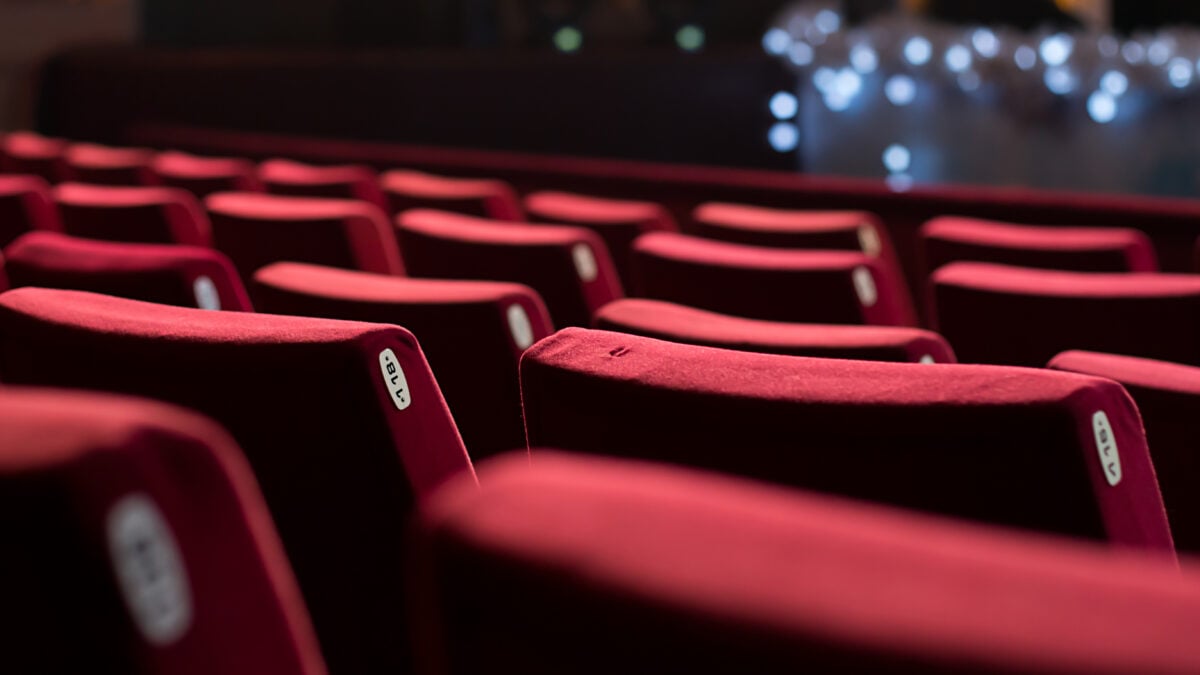 A rear view of rows of red velvet seats in an empty theatre