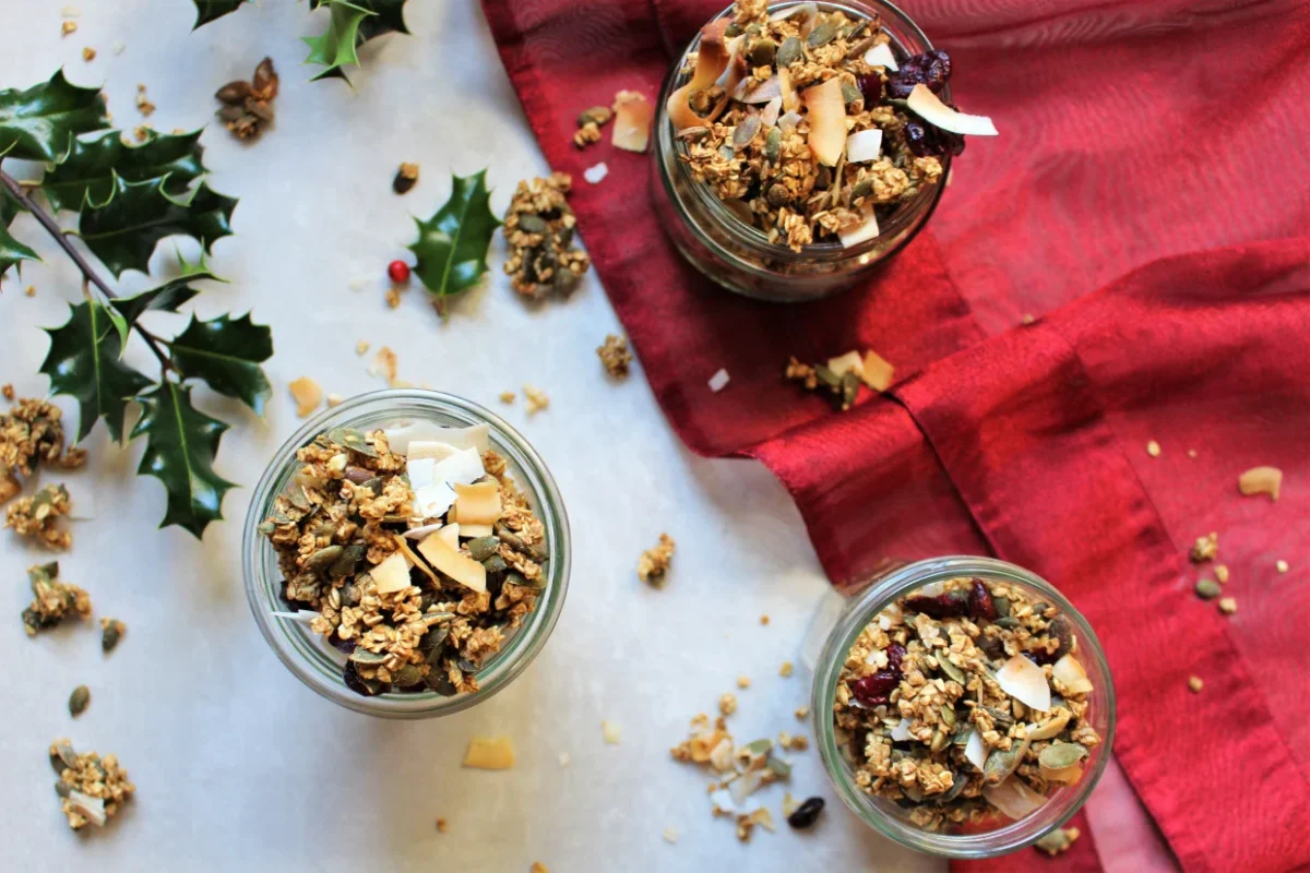 Photo shows three jars of vegan Christmas granola from above on a white and red tablecloth.