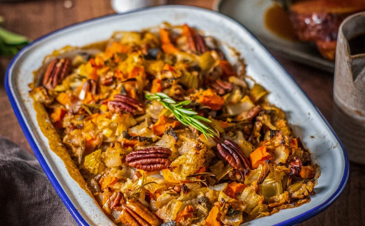 Photo shows a dish of pecan apple stuffing decorated with nuts and garnish.