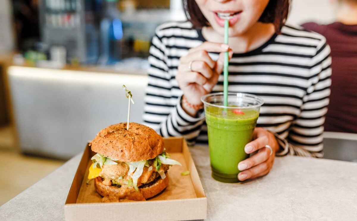 A woman drinking a green smoothie and eating a vegan burger
