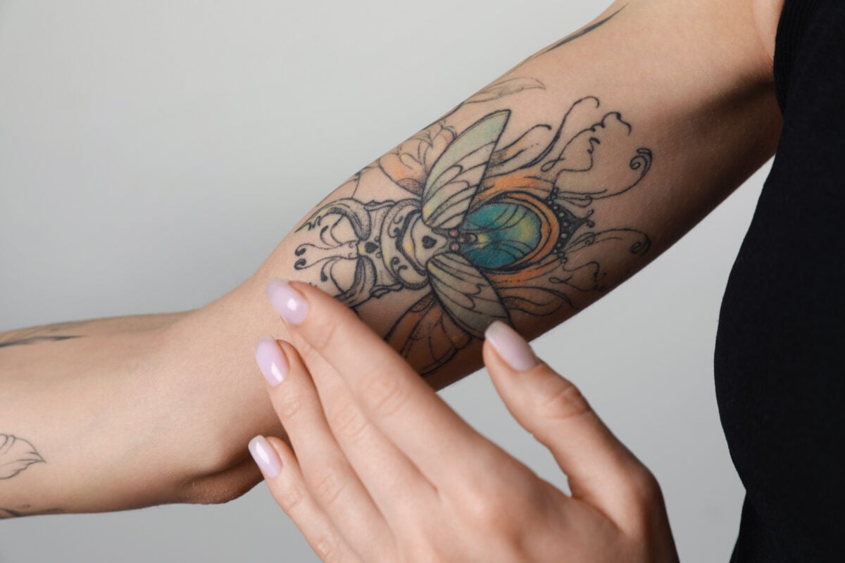 Photo shows a woman applying cream to a healing tattoo on her inner arm.