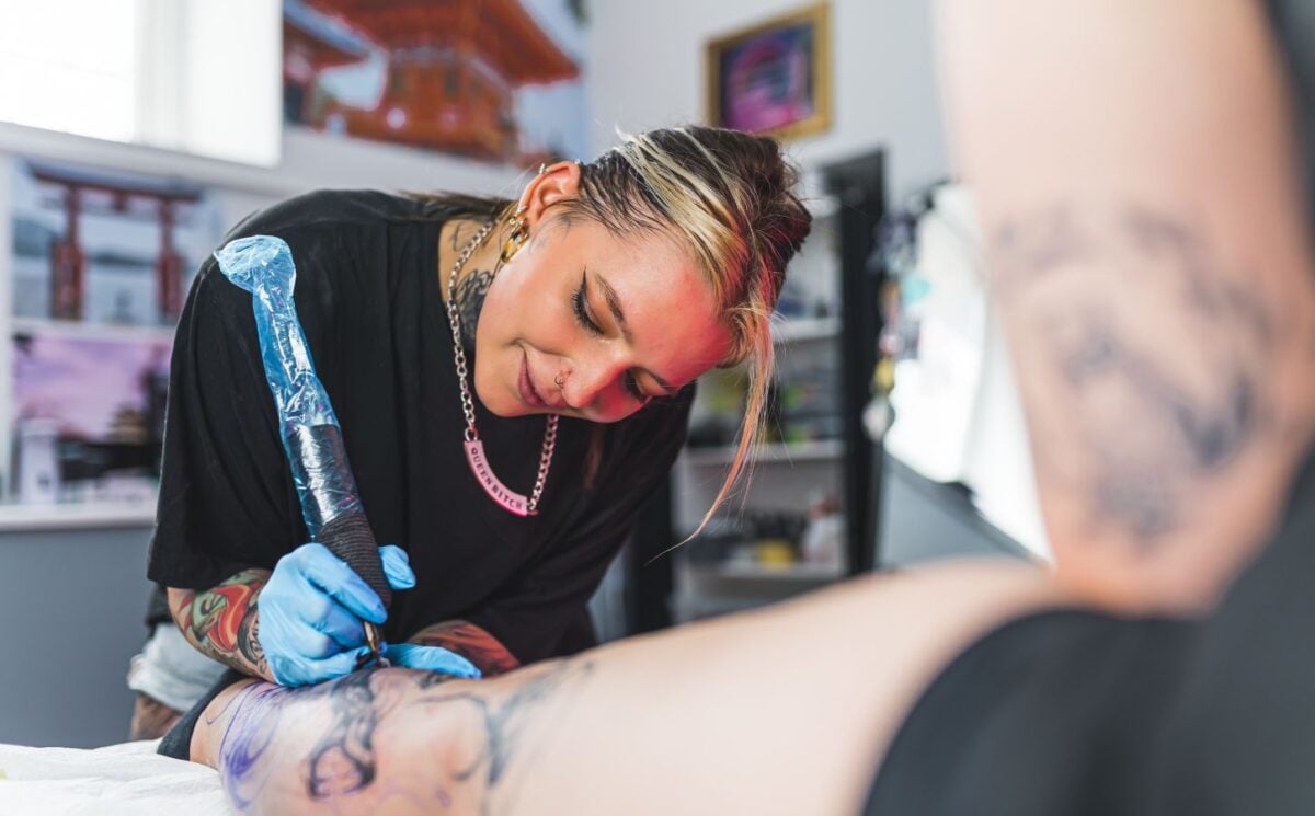 Photo shows a woman tattooing someone's leg.