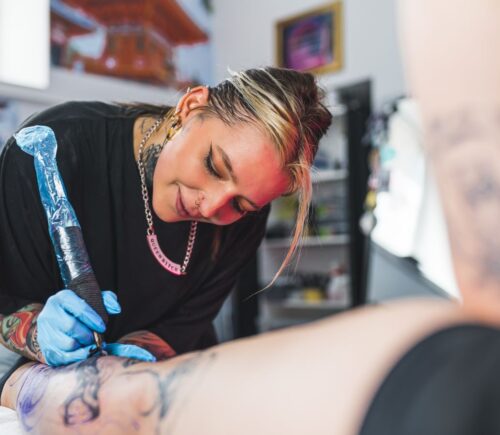 Photo shows a woman tattooing someone's leg.