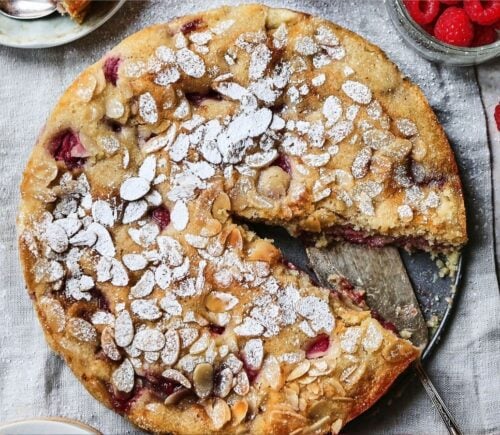 A whole vegan bakewell cake with a slice taken out of it