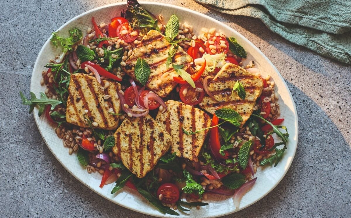 Photo shows a large bowl of salad topped with vegan halloumi.