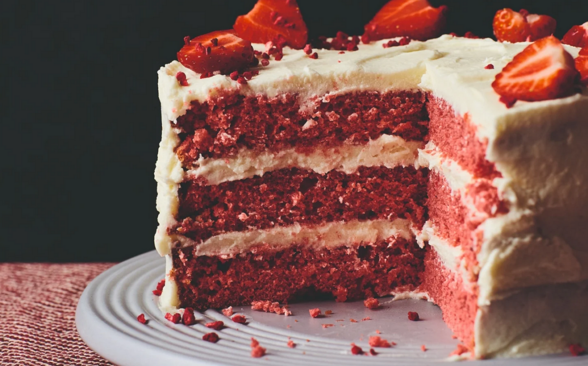 Photo shows a vegan red velvet cake topped with sliced strawberries.
