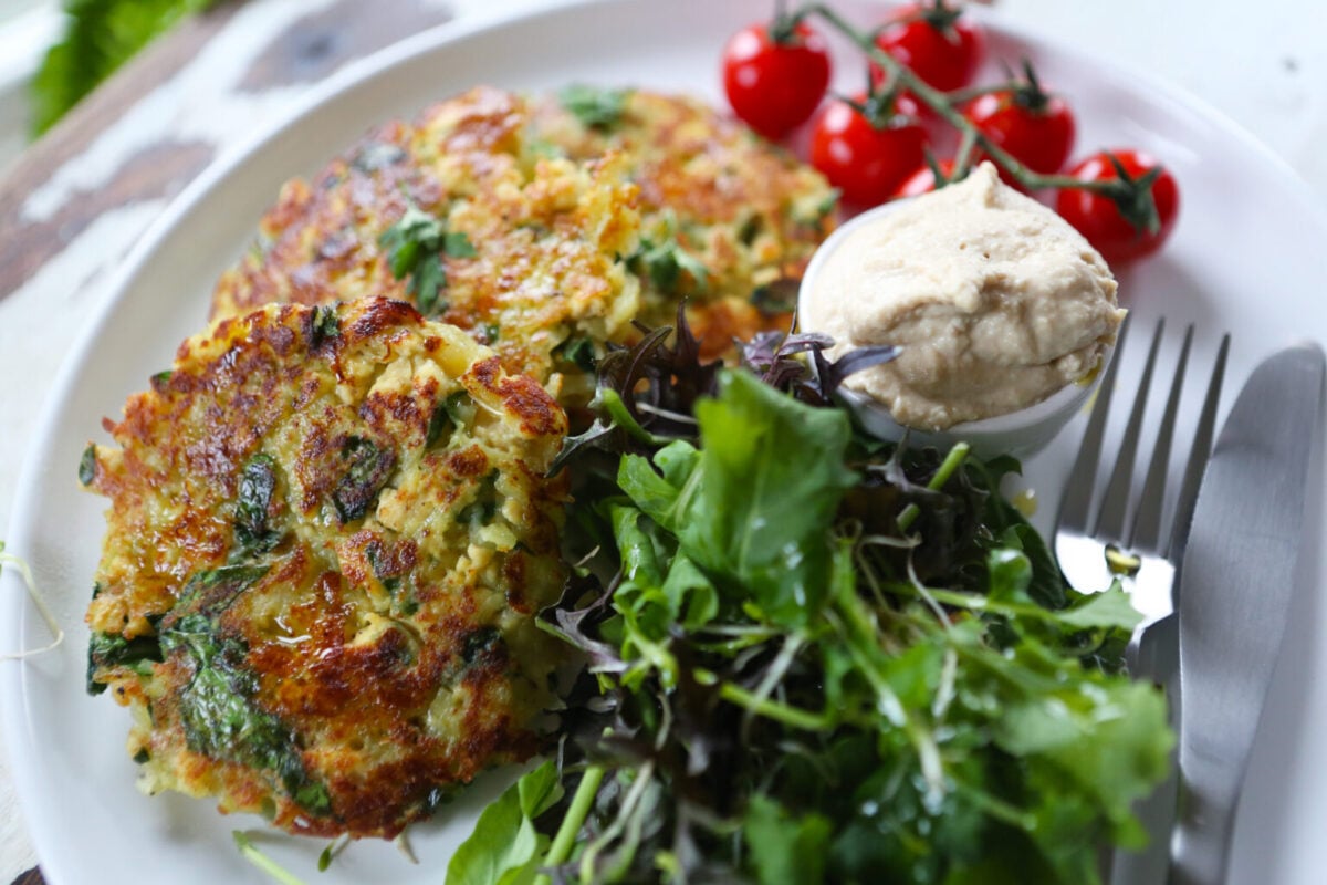 Photo shows a plate of spinach and potato rosti served with salad and hummus.
