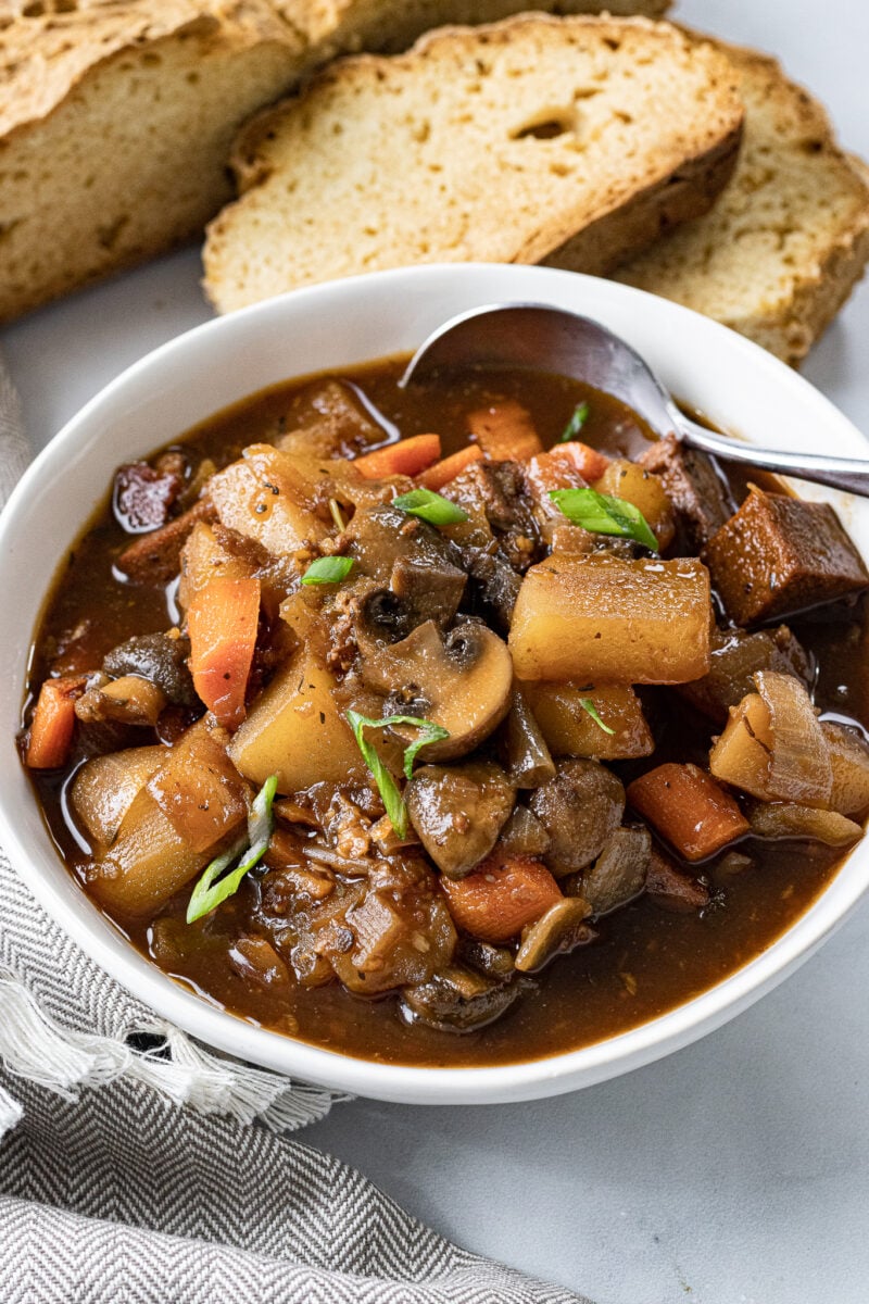A bowl of vegan beef stew made with plant-based ingredients next to some crusty bread