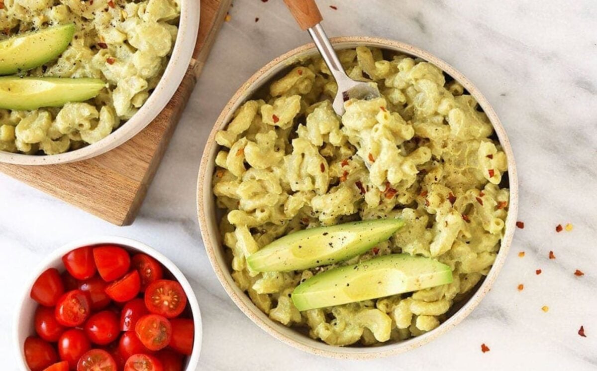 Photo shows two dishes of avocado-based mac and cheese with a side of tomatoes.
