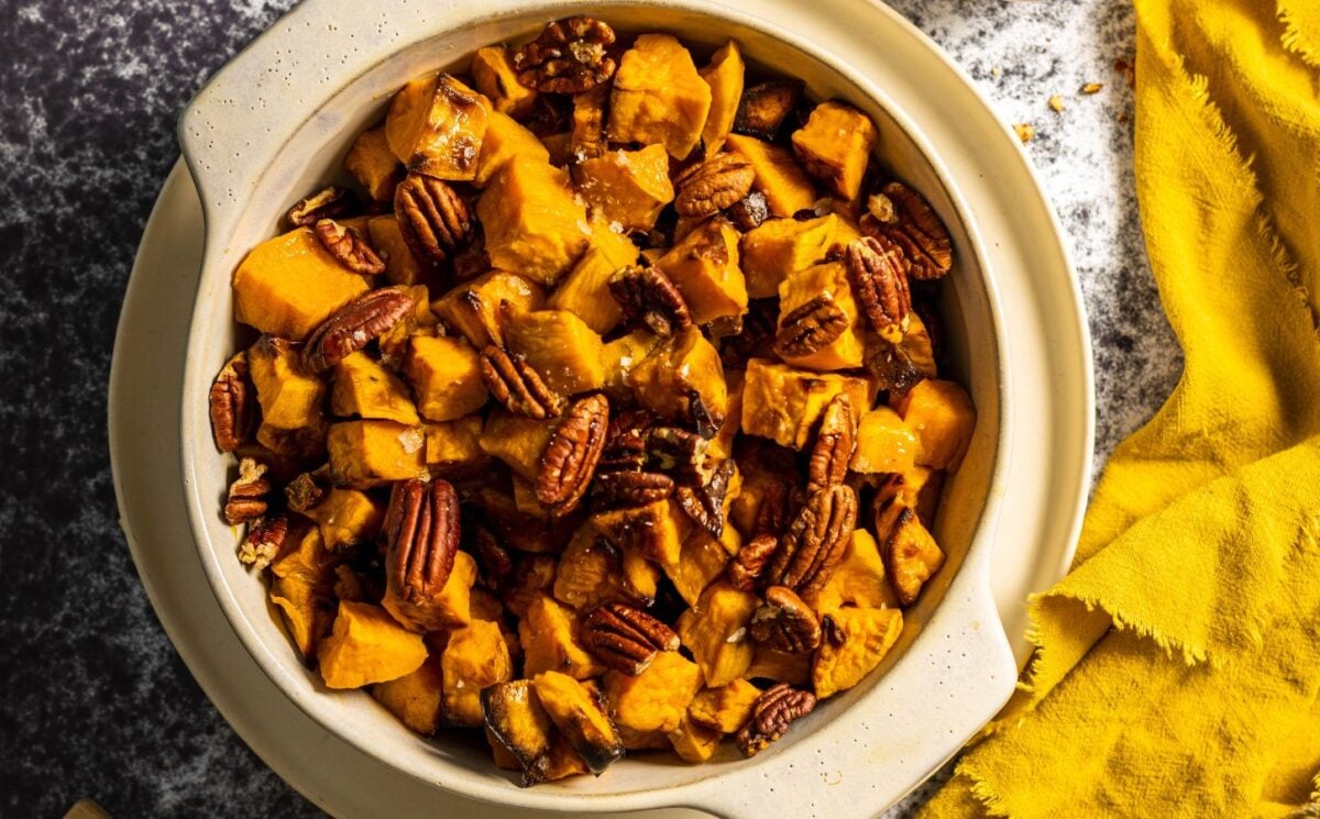 Photo shows a dish of maple-roasted sweet potatoes topped with pecan nuts.