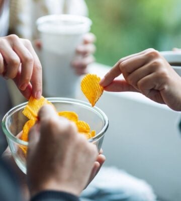 Photo shows three people standing together and reaching for the same bowl of crisps.