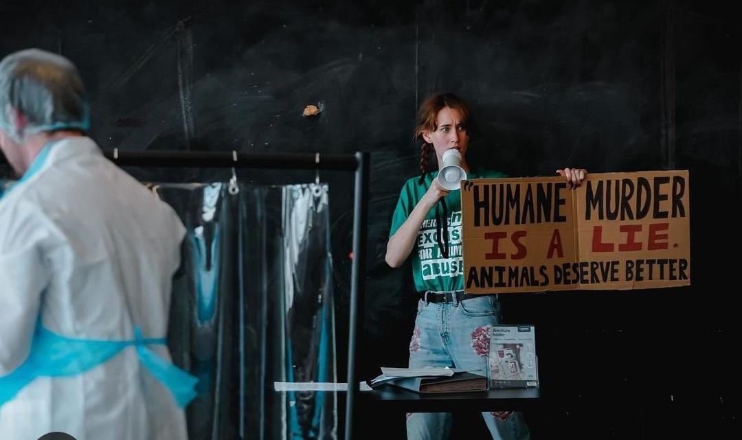 An actor holding up a sign saying "humane slaugher is a lie" in a new play about slaugherhouse work