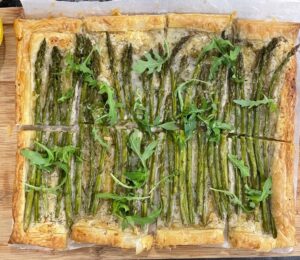 A vegan asparagus tart on a chopping board with a lemon and a knife next to it