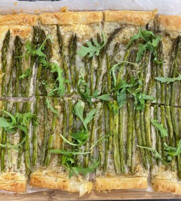 A vegan asparagus tart on a chopping board with a lemon and a knife next to it