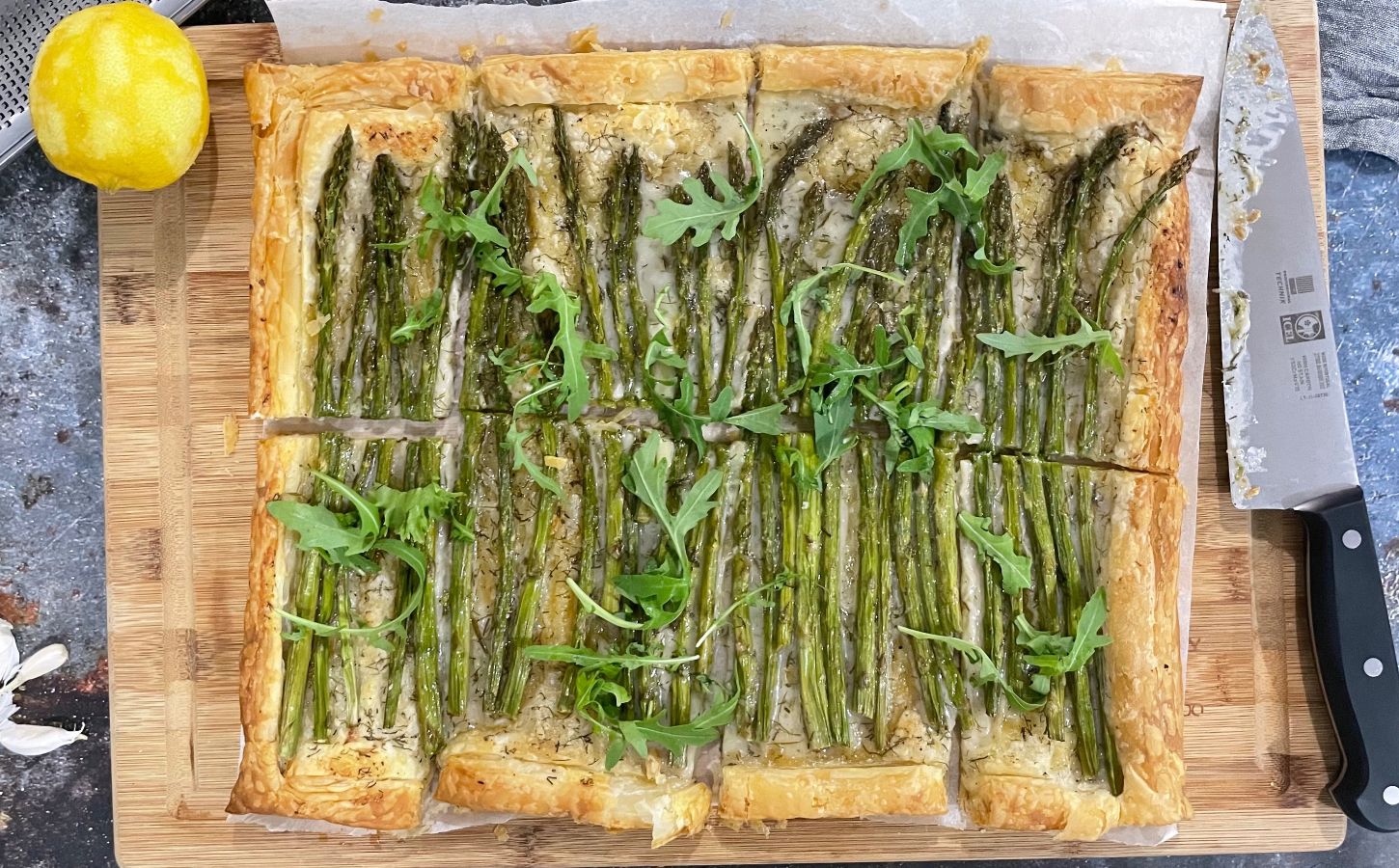 A vegan asparagus tart on a chopping board with a lemon and a knife next to it