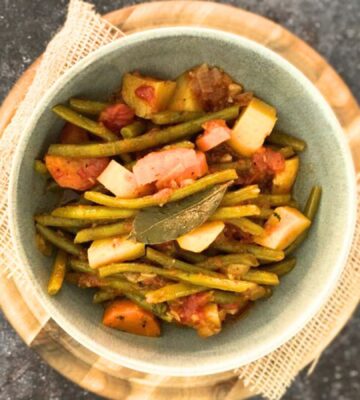 A bowl of green bean stew on top of a wooden board on a dark countertop