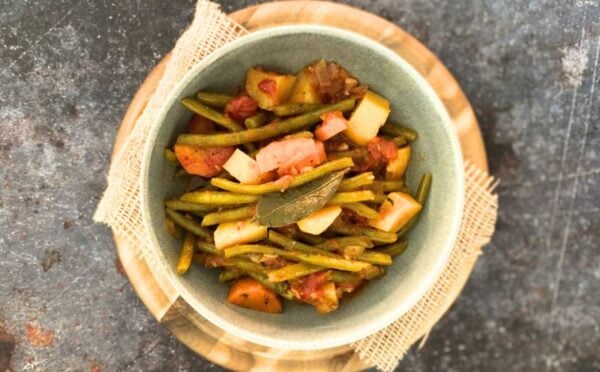 A bowl of green bean stew on top of a wooden board on a dark countertop