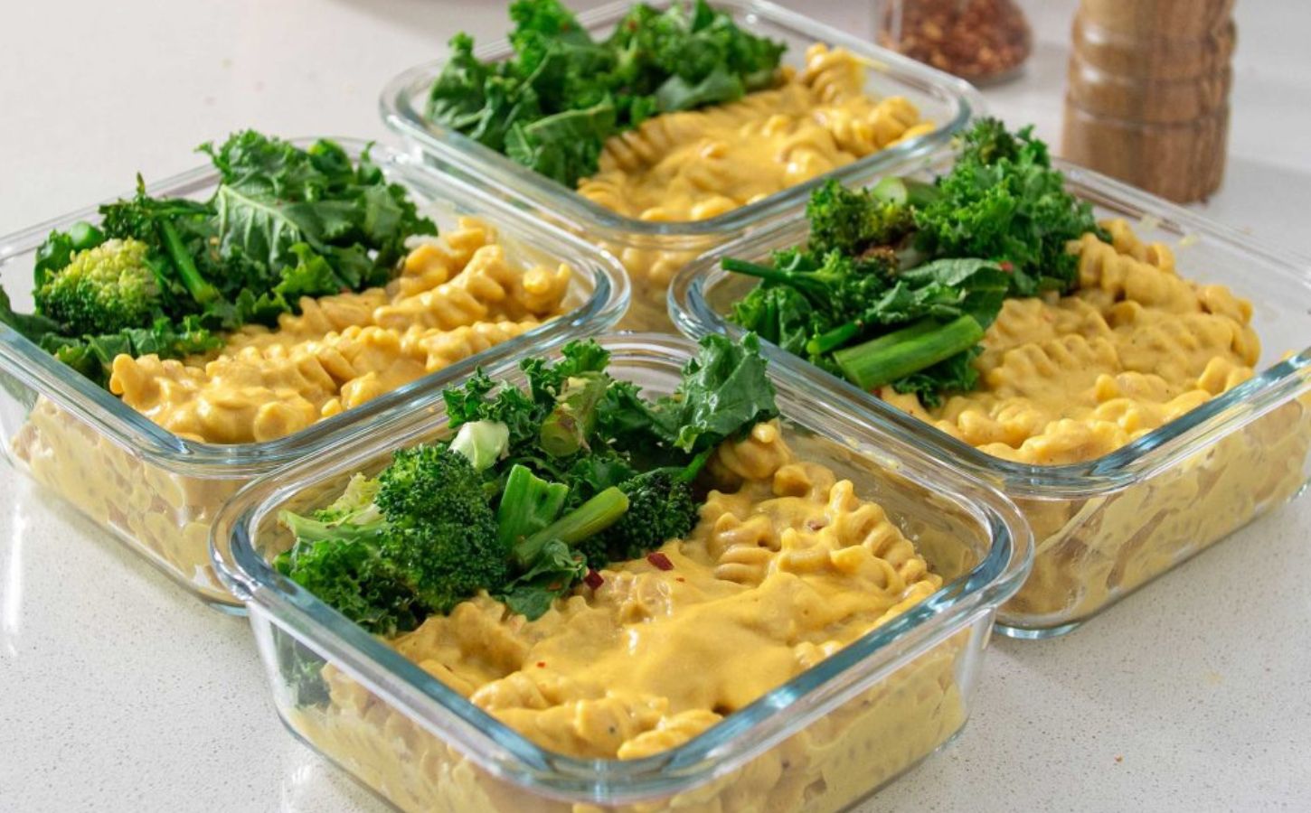 Four dishes of meal prepped high protein vegan mac and cheese with greens ontop
