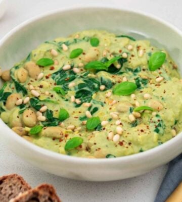 A bowl of vegan pesto butter beans next to some cutlery and bread