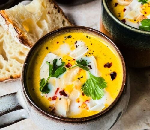 A mug of vegan Thai soup with coriander on top served next to bread