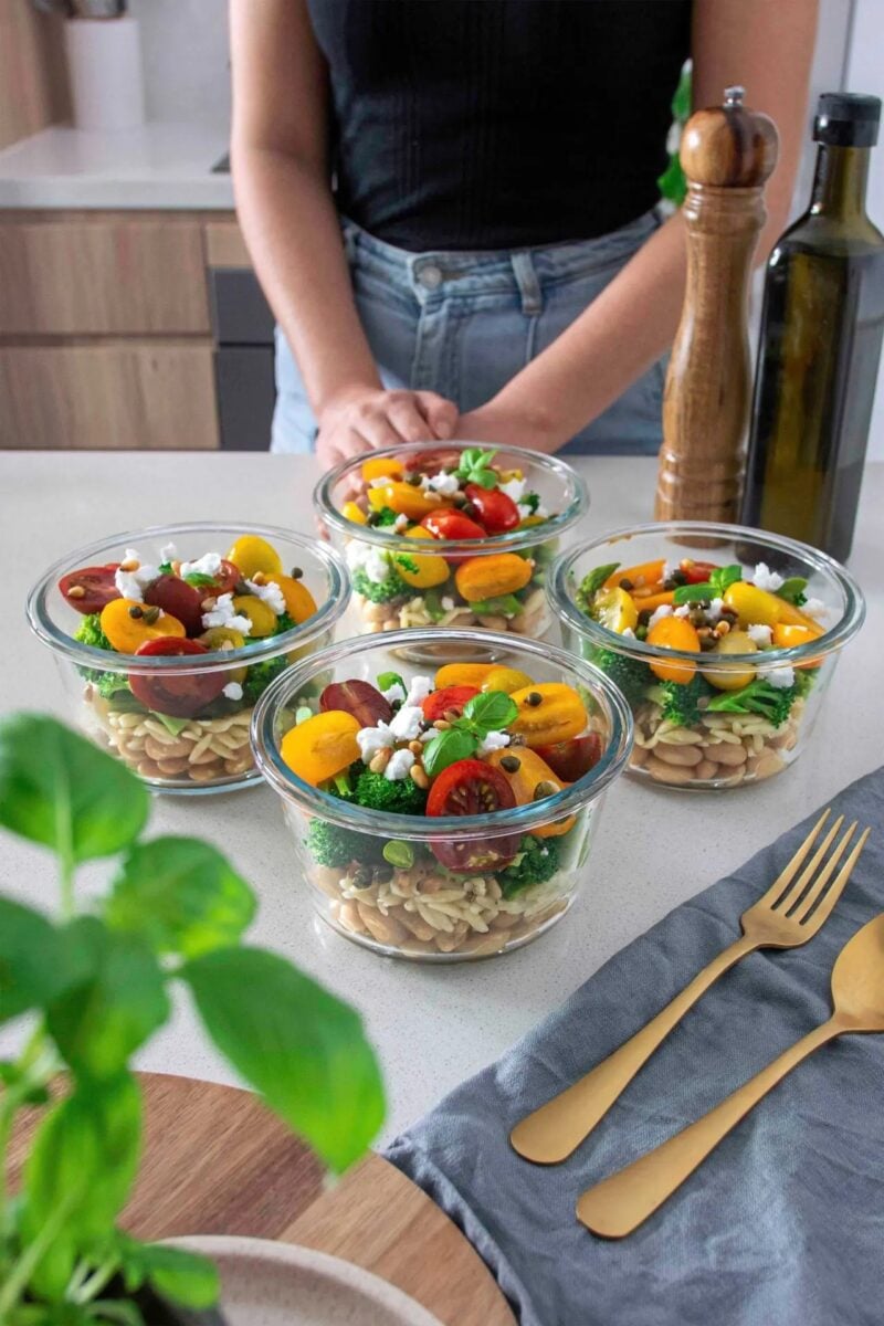 A vegan bean, orzo, pesto salad, all divided into separate containers for meal-prepping