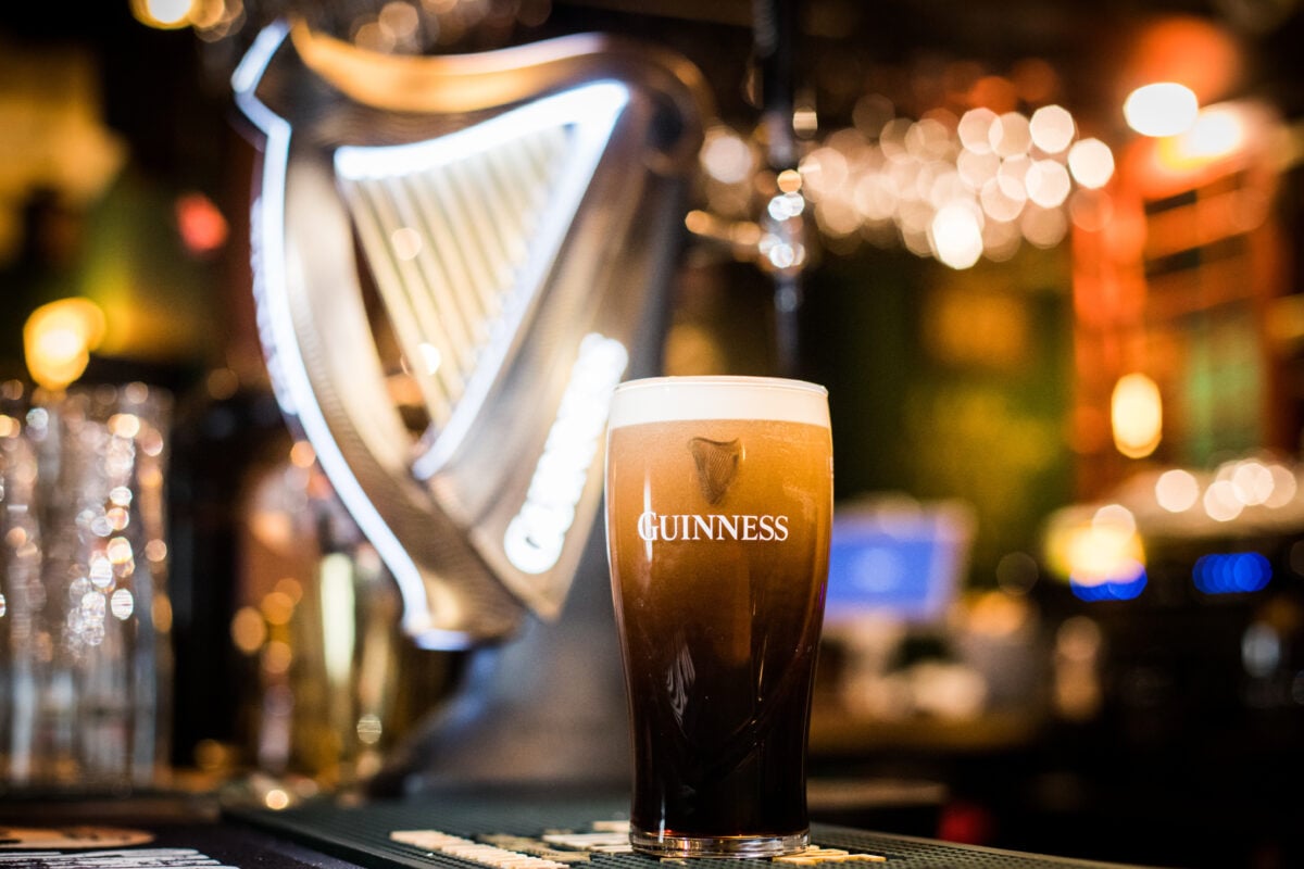 Photo shows a freshly poured pint of Guinness on a bar top next to a Guinness-branded pump.