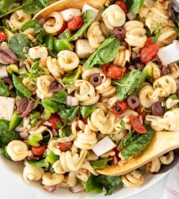 A Greek pasta salad made with dairy-free feta cheese, filled with tomatoes, olives, and spinach