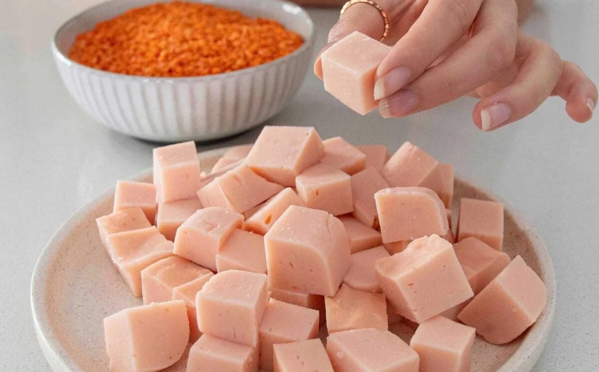 Photo shows someone taking the top piece from a white bowl of cubed red lentil tofu