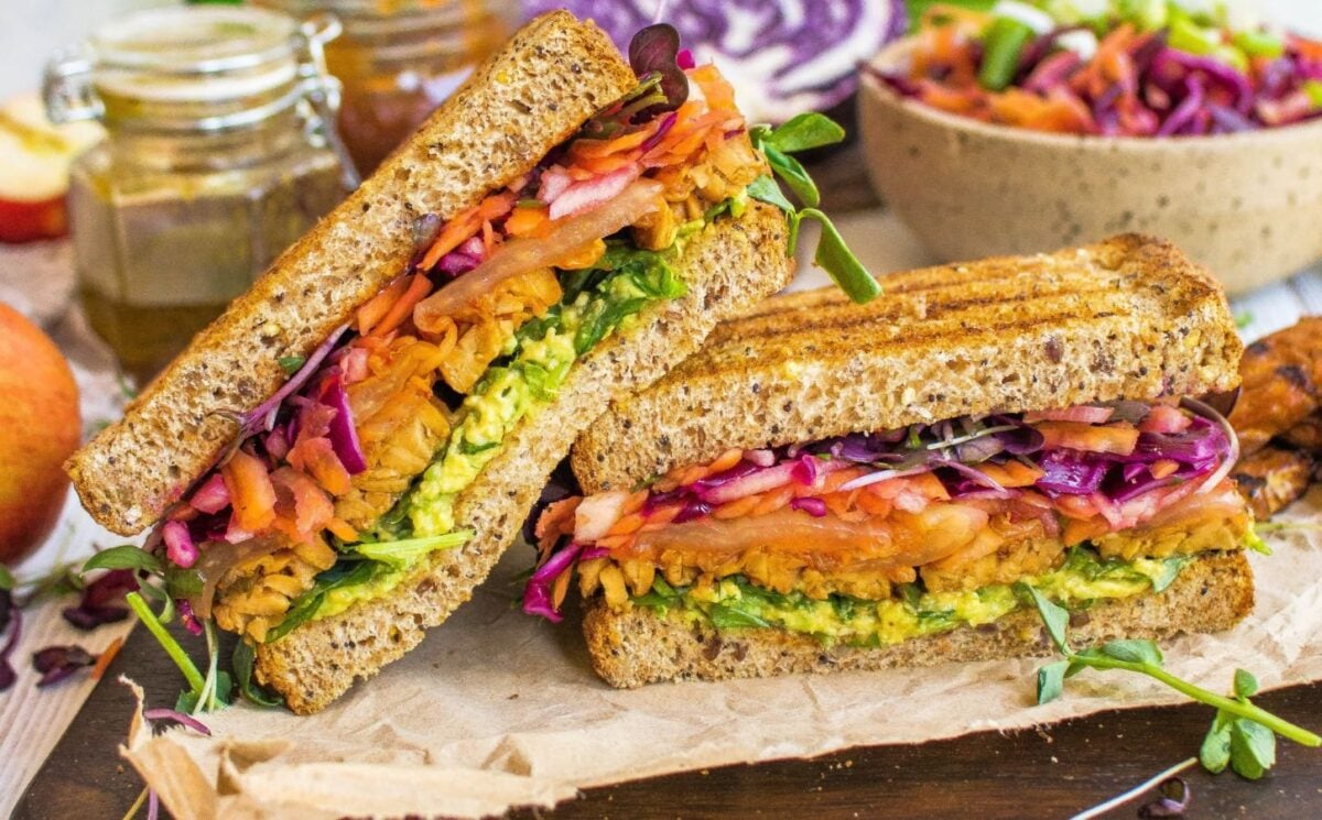 Photo shows a sandwich cut in half to reveal its filling of fresh apple slaw and thick pieces of marinated tempeh