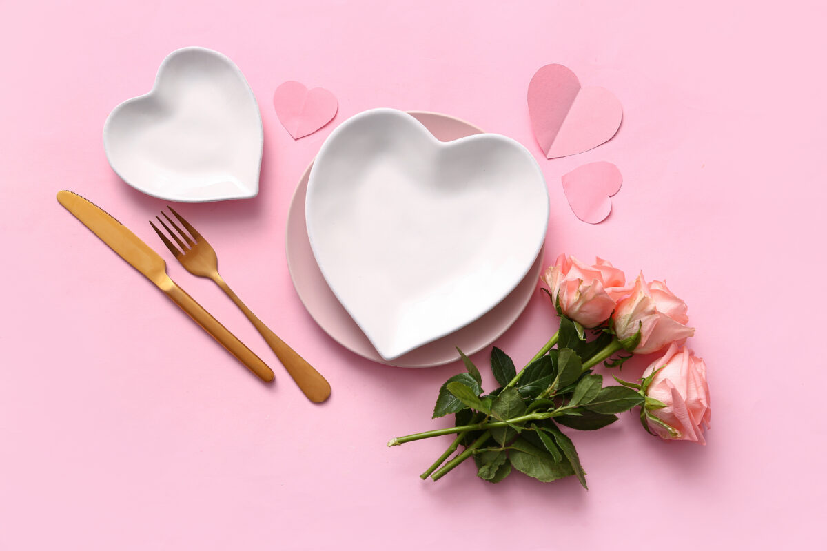 Heart-shaped plates next to a bunch of roses before a pink background, showcasing a vegan Valentine's Day meal deal