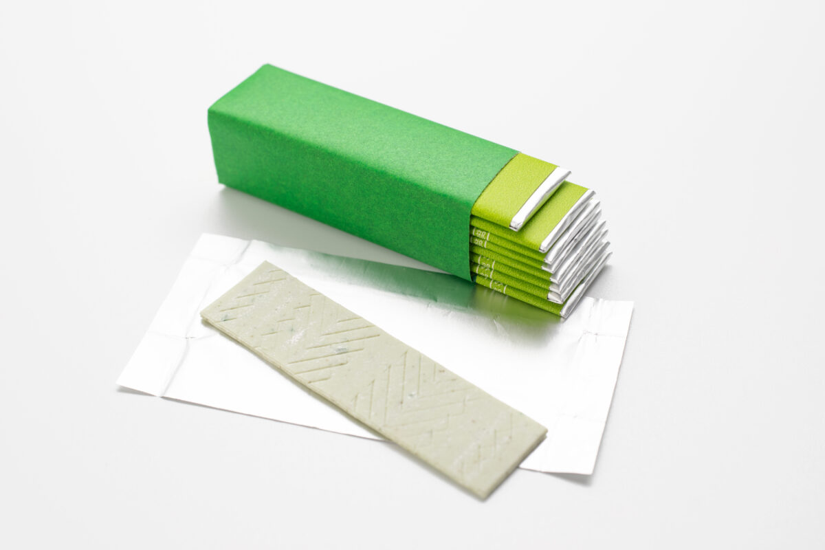 Photo shows an open, green pack of gum with individually foil-wrapped pieces visible inside on a white background