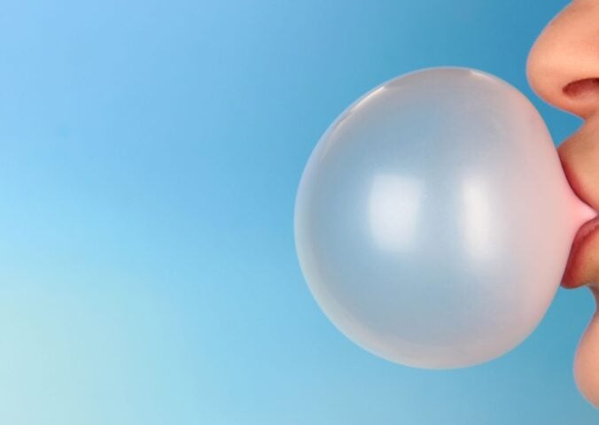 Photo shows part of someone's face (nose to chin) from the side as they blow a large pink bubble of chewing gum