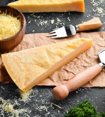 Photo shows a wedge of parmesan, an Italian hard cheese, on a board alongside a grater and small fork