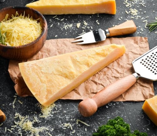 Photo shows a wedge of parmesan, an Italian hard cheese, on a board alongside a grater and small fork