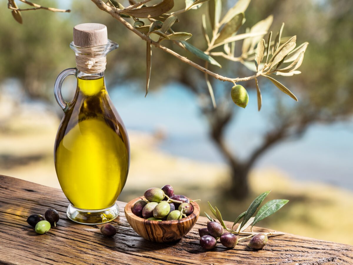 A bottle of olive oil next to some olives