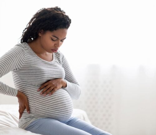A pregnant woman sitting on a bed holding her bump