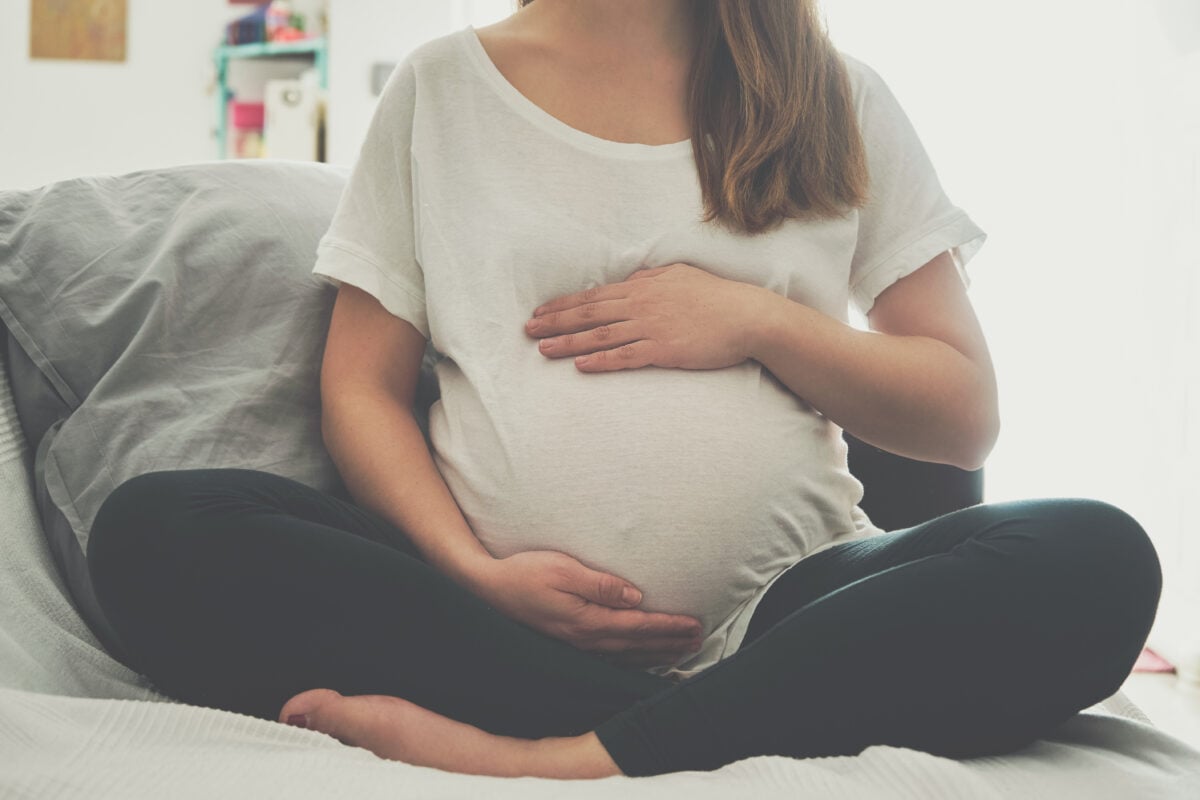 A pregnant woman holding her bump while sat on a bed