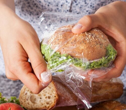 Photo shows someone's hands as they wrap a sandwich in a plastic Ziploc-style sandwich bag