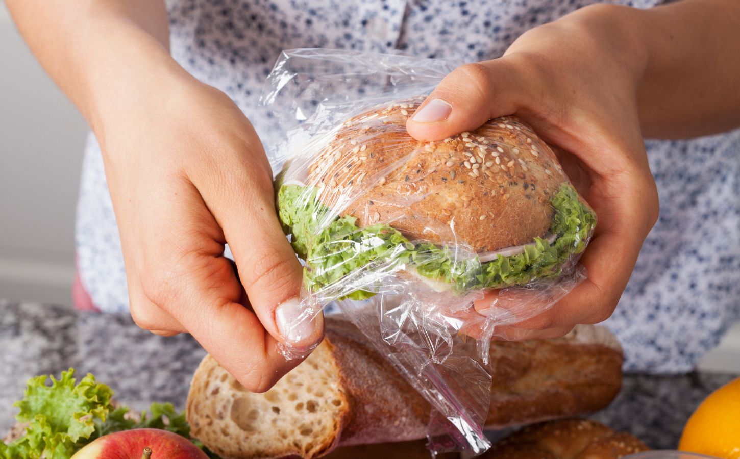 Photo shows someone's hands as they wrap a sandwich in a plastic Ziploc-style sandwich bag