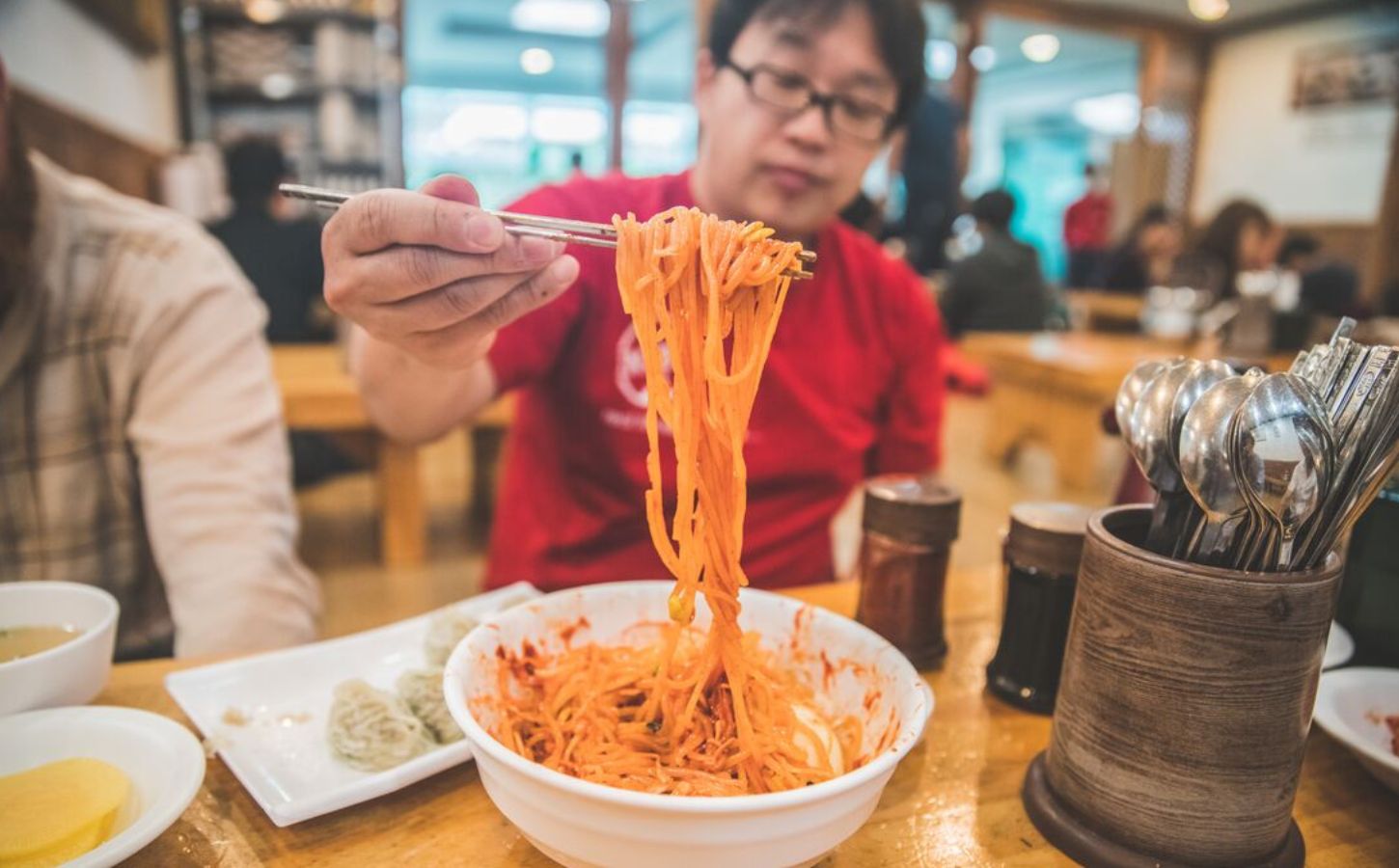 Photo shows a man holding up noodles over a bowl using chopsticks