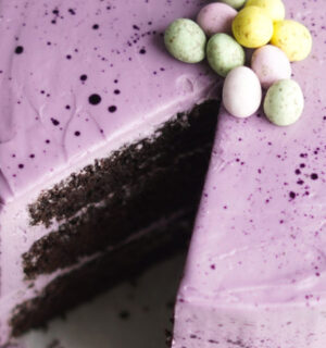 Moist vegan Easter chocolate cake with layers of purple vegan vanilla frosting and decorated with vegan mini eggs