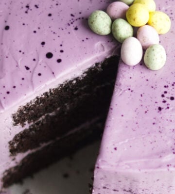 Moist vegan Easter chocolate cake with layers of purple vegan vanilla frosting and decorated with vegan mini eggs