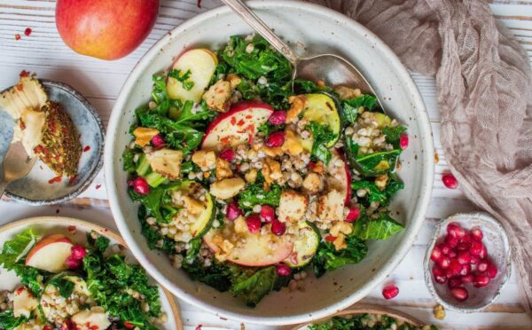 Photo shows Happy Skin Kitchen's kale and apple salad in a large pale bowl alongside smaller bowls with the component ingredients in