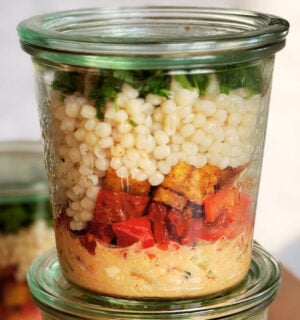vegan couscous salad jar with pearl couscous, hummus, tofu, harissa spice, and assorted vegetables