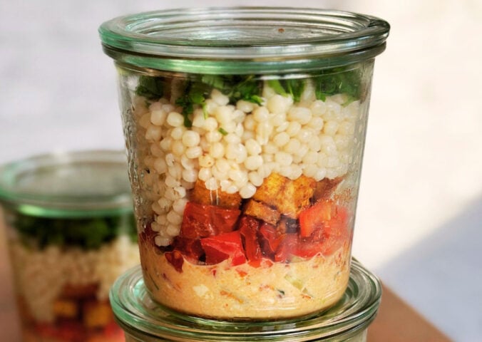 vegan couscous salad jar with pearl couscous, hummus, tofu, harissa spice, and assorted vegetables