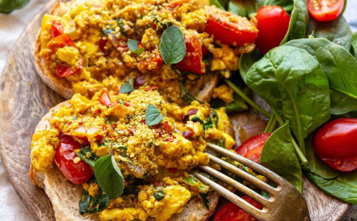 Photo shows a close-up of a tofu scramble topped with spinach and tomatoes