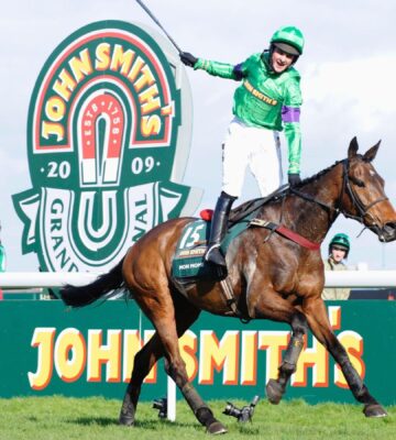 A person whipping a horse at the Grand National